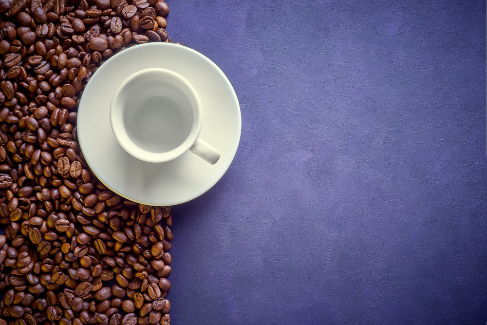taza de cafe y granos de cafe en fondo lila